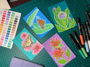 A spread of small illustrations from the Butterfly Gardens series, surrounded by markers and other drawing tools.