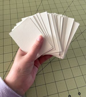 Maggie's hand holding a stack of small blank pieces of paper, spread out like a deck of cards.